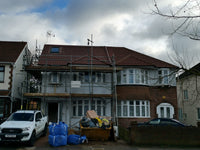 House under construction with scaffolding and materials on a cloudy day.