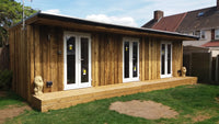 Wooden garden room with glass doors and windows on a grassy area.