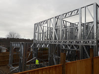 Metal frame structure under construction with a person in a yellow vest in the background.