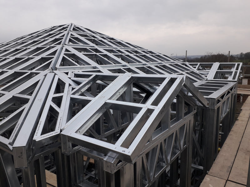 Metal roof trusses on a construction site with a cloudy sky.