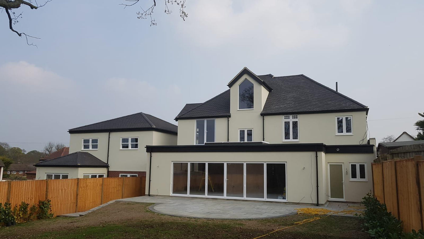 Newly built house with modern design and large windows, surrounded by a wooden fence.