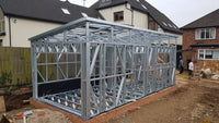 Metal frame structure of a building under construction with residential houses in the background.