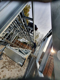 Metal frame structure with a person working on it, possibly a roof or building framework.