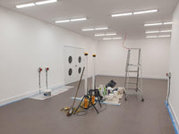 Empty room with white walls, gray floor, ladder, and painting supplies.