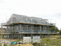 Building under construction with scaffolding and exposed framework against a cloudy sky.