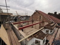 Construction site with large metal beams and scaffolding against a cloudy sky.