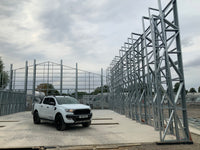 White pickup truck parked in front of a partially constructed metal building frame.