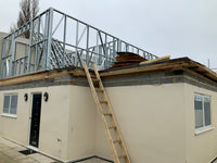 Building under construction with a metal roof frame and wooden ladder.