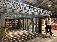 Person working on a metal framework structure in a warehouse.