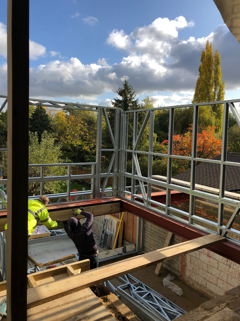 Construction site with metal frame and person in yellow jacket against a blue sky with clouds.