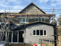 House under construction with scaffolding and visible insulation on a clear day.
