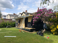 House extension under construction with a ladder and tools on a grassy lawn.