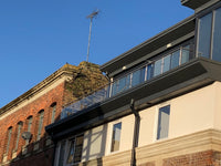 Building exterior with modern roofline and glass balustrade against a clear blue sky.