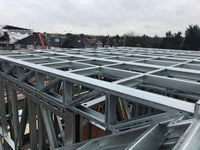 Metal roof trusses on a construction site with a cloudy sky.