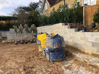 Construction site with a partially built wall and materials in a backyard.