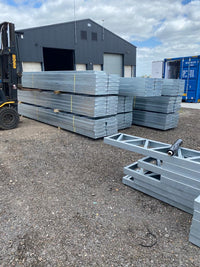 Stacks of metal sheets on a gravel surface with a building in the background