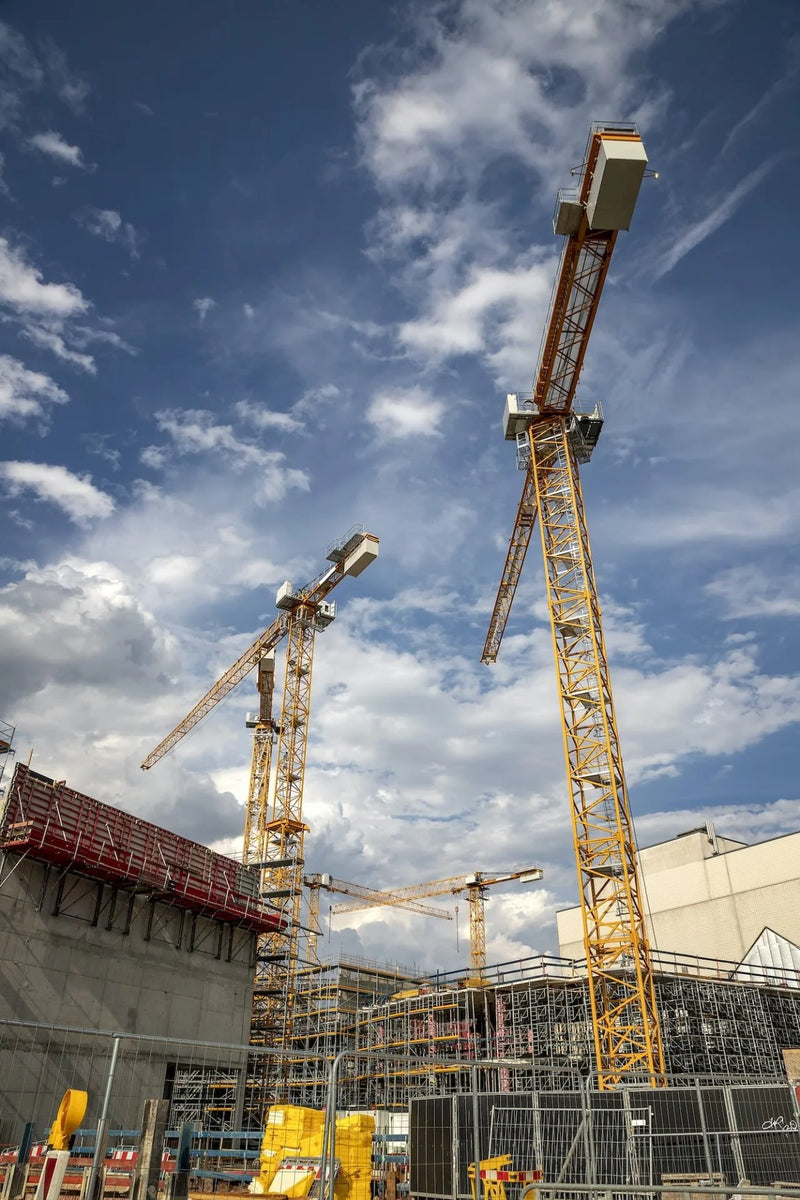 Construction site with multiple cranes against a blue sky with clouds