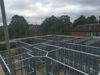 Steel frame structure of a building under construction with trees and a building in the background.