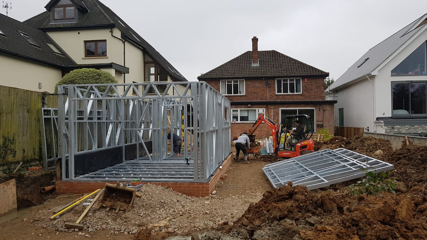 Construction site with a metal frame house and workers in a residential area.